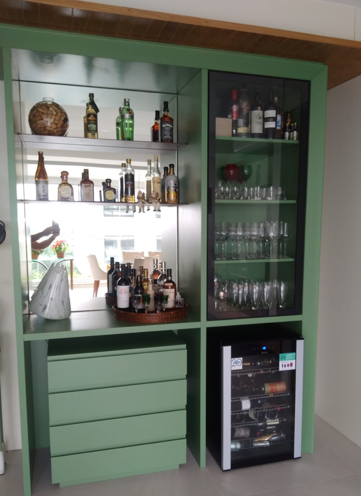 Bar em verde com prateleiras espelhadas, vitrine de taças e adega climatizada